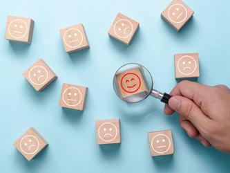 Hand with magnifying glass over a wooden block with a smiley face